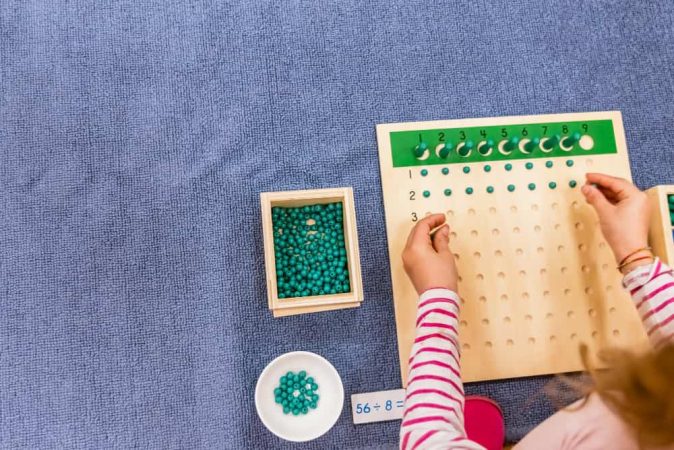 Une enfant utilise un tableau de calcul pour résoudre une division, illustrant des Jeux de Réflexion Montessori.