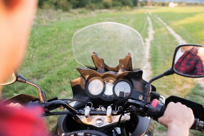 Vue subjective d'un motard en chemise à carreaux conduisant une moto avec un pare-brise Yamaha sur un chemin rural.