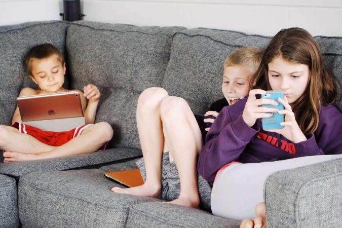 Écrans aux jeunes enfants : des enfants absorbés par leurs tablettes et smartphones sur un canapé.