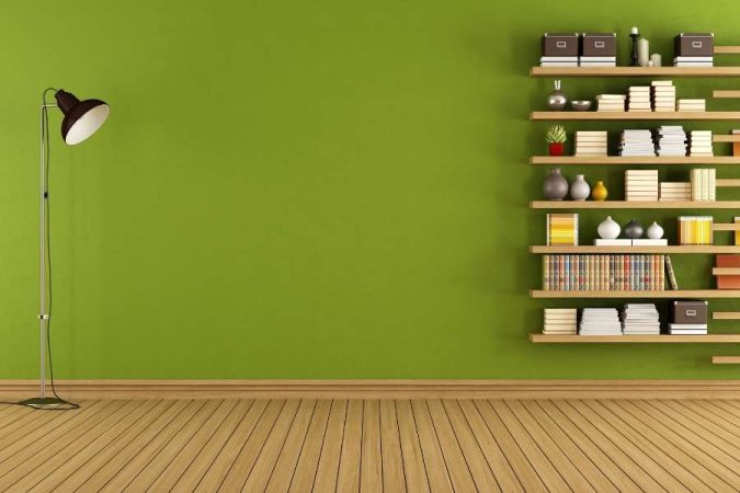 Une bibliothèque murale composée d'étagères en bois remplies de livres et de bibelots, fixée sur un mur vert olive