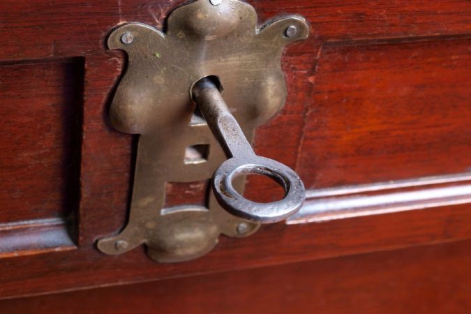 Une vieille clé métallique est insérée dans l'entrée de serrure en laiton ouvragée d'un meuble en bois, illustrant l'étape pour remplacer une serrure de meuble ancienne.